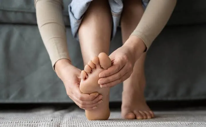 A person sitting down easing the sole of their foot — working on relief from burning, tingling foot neuropathy