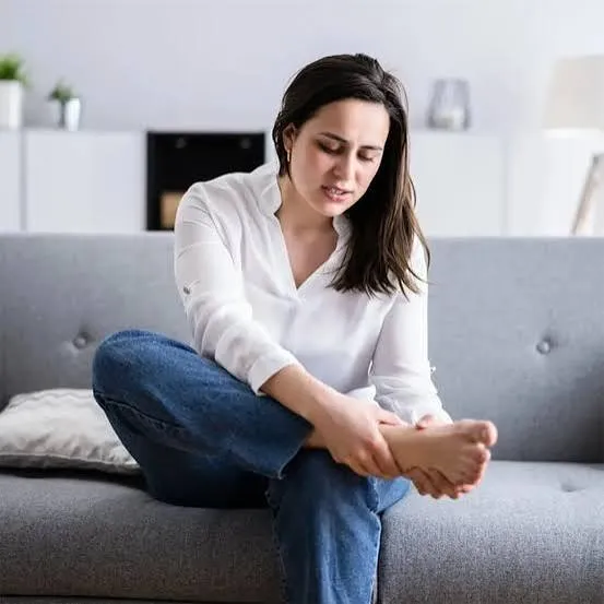 A woman sitting at home holding her foot, easing the burning and tingling of nerve discomfort